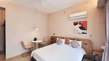 Une chambre d’hôtel avec un lit, un ventilateur de plafond, une petite table avec une chaise, un appareil de climatisation et un tableau au mur.