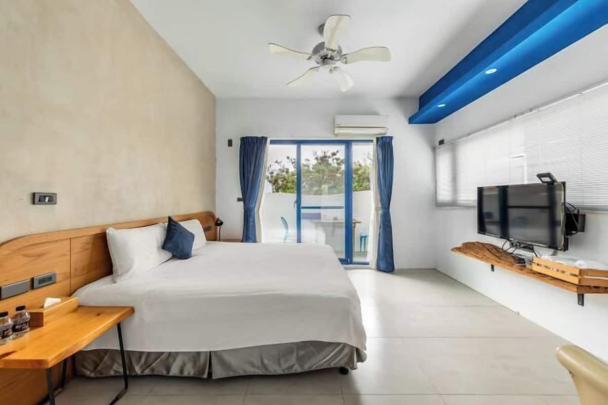 A modern hotel room with a bed, a desk, a television, and a ceiling fan.