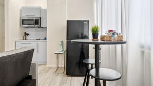 A modern kitchen with a black refrigerator, white cabinets, and a microwave. There is a small table with a potted plant and a basket. - Central Condado Trendy Escape (San Juan)