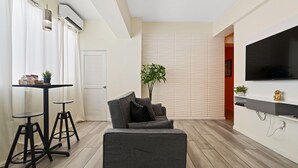 A modern living room with a grey sofa, two black bar stools, a small table with a potted plant, and a flat-screen TV mounted on the wall. - Central Condado Trendy Escape (San Juan)
