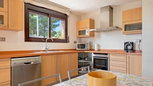 A modern kitchen with wooden cabinets, a dishwasher, microwave, oven, and a window with curtains. - Holiday Home 'Casa Tico' with Private Pool, Wi-Fi (Roda De Bara)
