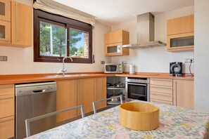 A modern kitchen with wooden cabinets, a dishwasher, microwave, oven, and a window with curtains. - Holiday Home 'Casa Tico' with Private Pool, Wi-Fi (Roda De Bara)