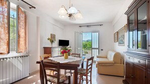 A dining area with a table, chairs, a vase of flowers, a television, and a sofa. - Apartment 'Da Dri´' with Private Terrace, Private Garden and Balcony (Brugnato)