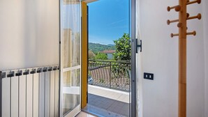 A balcony with a view of greenery and a distant building, a radiator, and a wooden coat rack. - Apartment 'Da Dri´' with Private Terrace, Private Garden and Balcony (Brugnato)