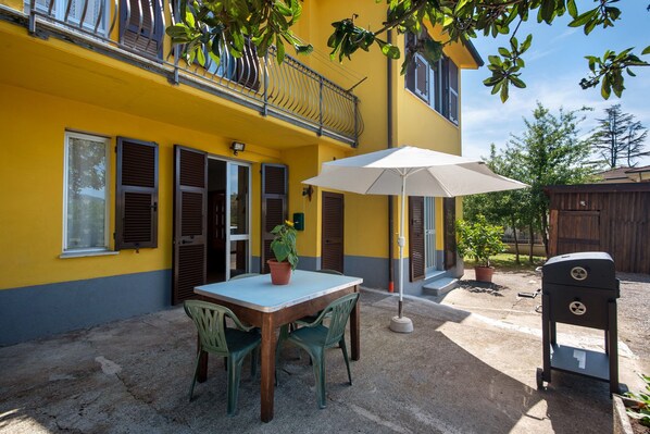 A yellow building with a balcony, a table with chairs, a potted plant, and a grill.