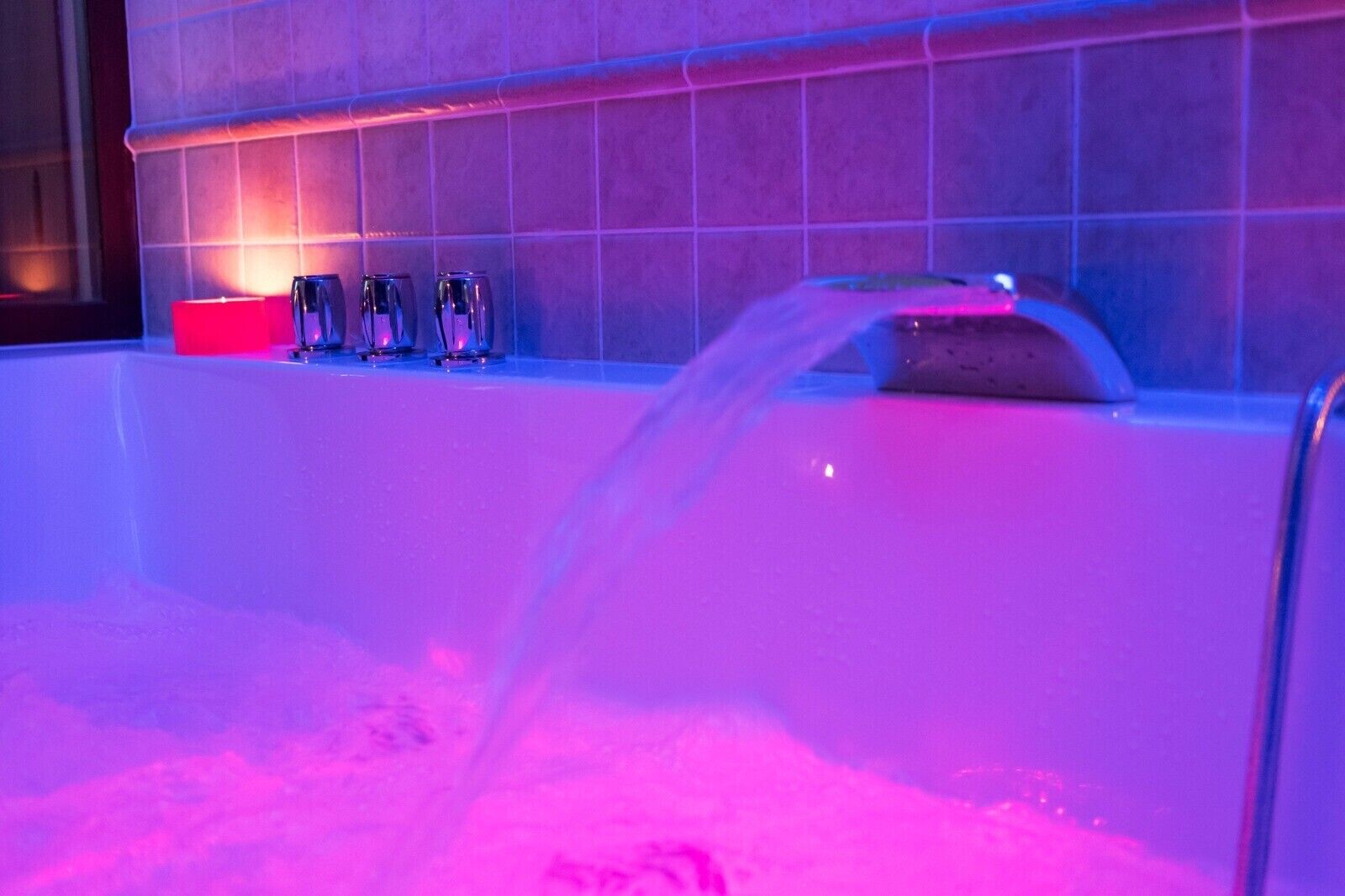 Eine Badewanne mit fließendem Wasser, eine rote Kerze und drei Gläser an einer gefliesten Wand.