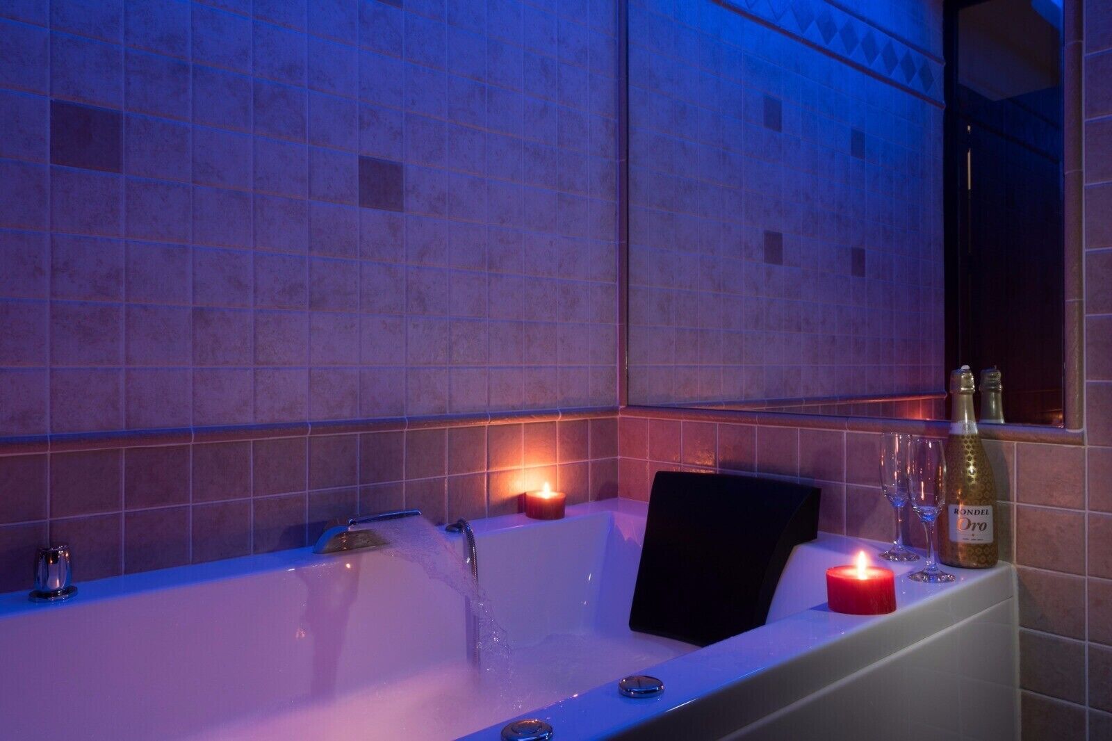 Un baño con una bañera, una vela y una botella de vino.