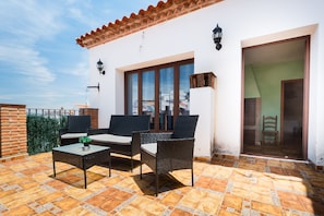 A patio with wicker furniture, a tiled floor, and a white building with a tiled roof. - Holiday Home 'Esencia Del Paladin' with Mountain Views (Zufre)