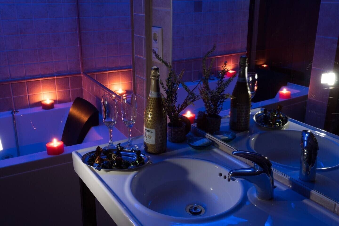 A bathroom with a bathtub, two sinks, a mirror, and decorative candles.
