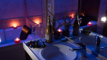 A bathroom with a bathtub, two sinks, a mirror, and decorative candles.
