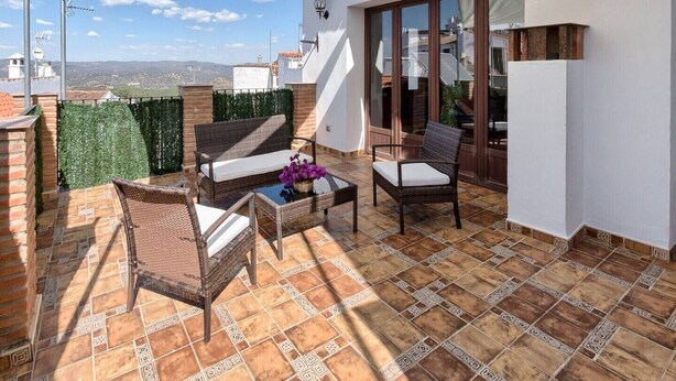 Una terrazza con mobili in vimini, un tavolo in vetro e vista sulla città.