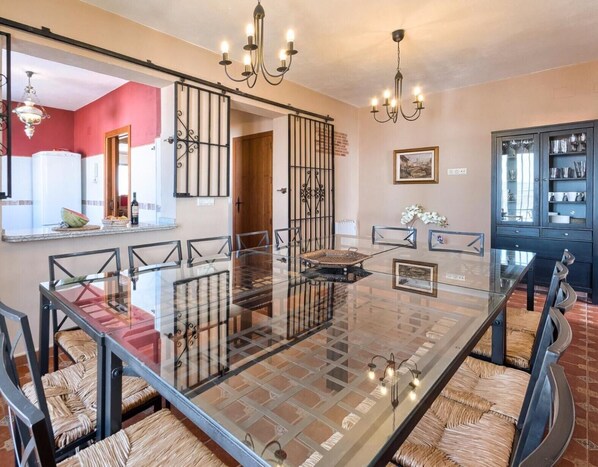A dining area with a glass-top table, woven chairs, a chandelier, and a kitchen cabinet in the background.