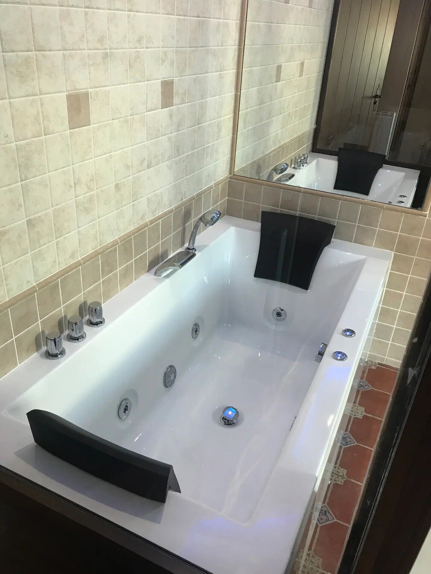 Een badkamer met een groot bad, een spiegel en betegelde wanden.