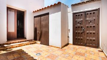 Un patio con suelo de baldosas, una puerta de madera y una pared blanca.