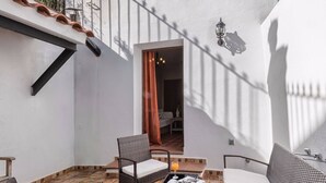 A patio with wicker furniture, a tiled floor, and a white wall with a door leading to an interior space.