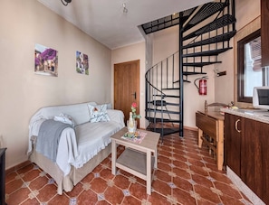 Sala de estar com sofá, uma mesinha, escada em espiral e área de cozinha.