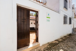 Um edifício branco com porta de madeira, uma janela pequena e uma placa na parede.