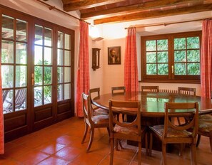 Ein Esszimmer mit einem runden Tisch, Holzsesseln, einem Fenster mit Blick ins Grüne und einer Tür mit Glasscheiben.