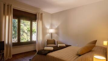 Habitació d'hotel amb llit, cadira, taula, làmpada i finestra amb cortines.