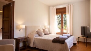 Un dormitorio con cama, lámparas de noche, televisor y ventana con cortinas.