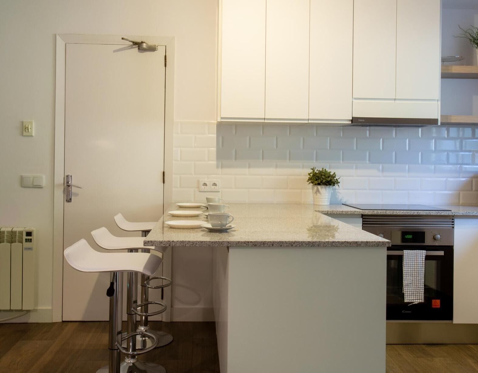 Une cuisine moderne avec des meubles blancs, un plan de travail en granit, un four encastré et un tabouret de bar.