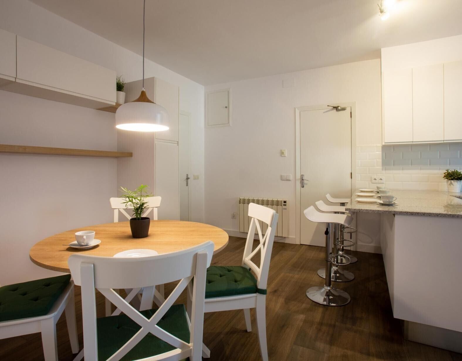 Una cocina moderna con armarios blancos, una mesa de comedor de madera y sillas con acolchado verde.
