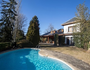 A house with a swimming pool, a covered patio, and a well-maintained lawn.