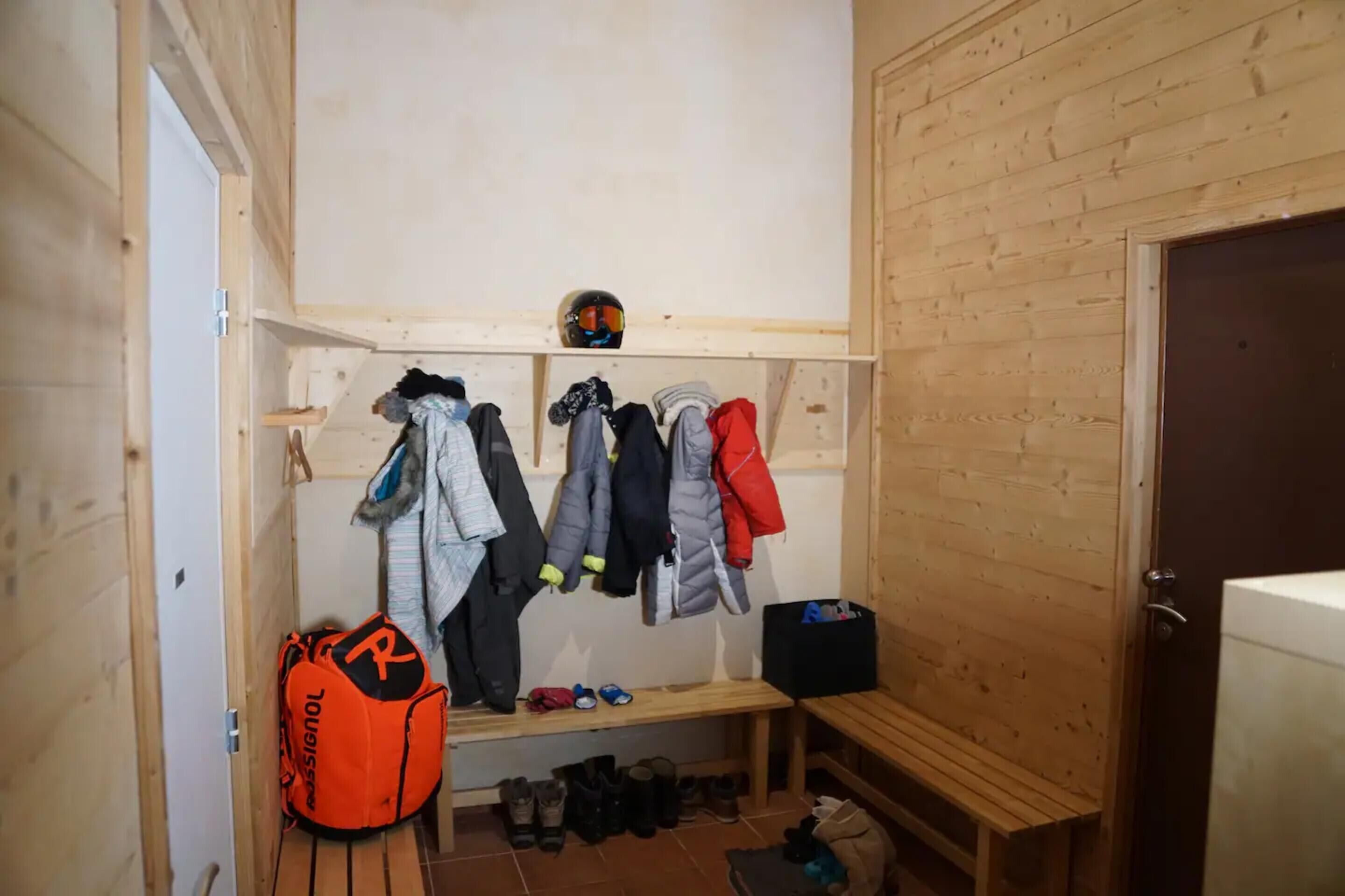 A wooden interior with a bench, a shelf with helmets, and a rack of jackets.
