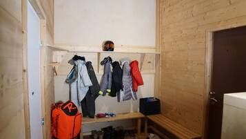 A wooden interior with a bench, a shelf with helmets, and a rack of jackets.
