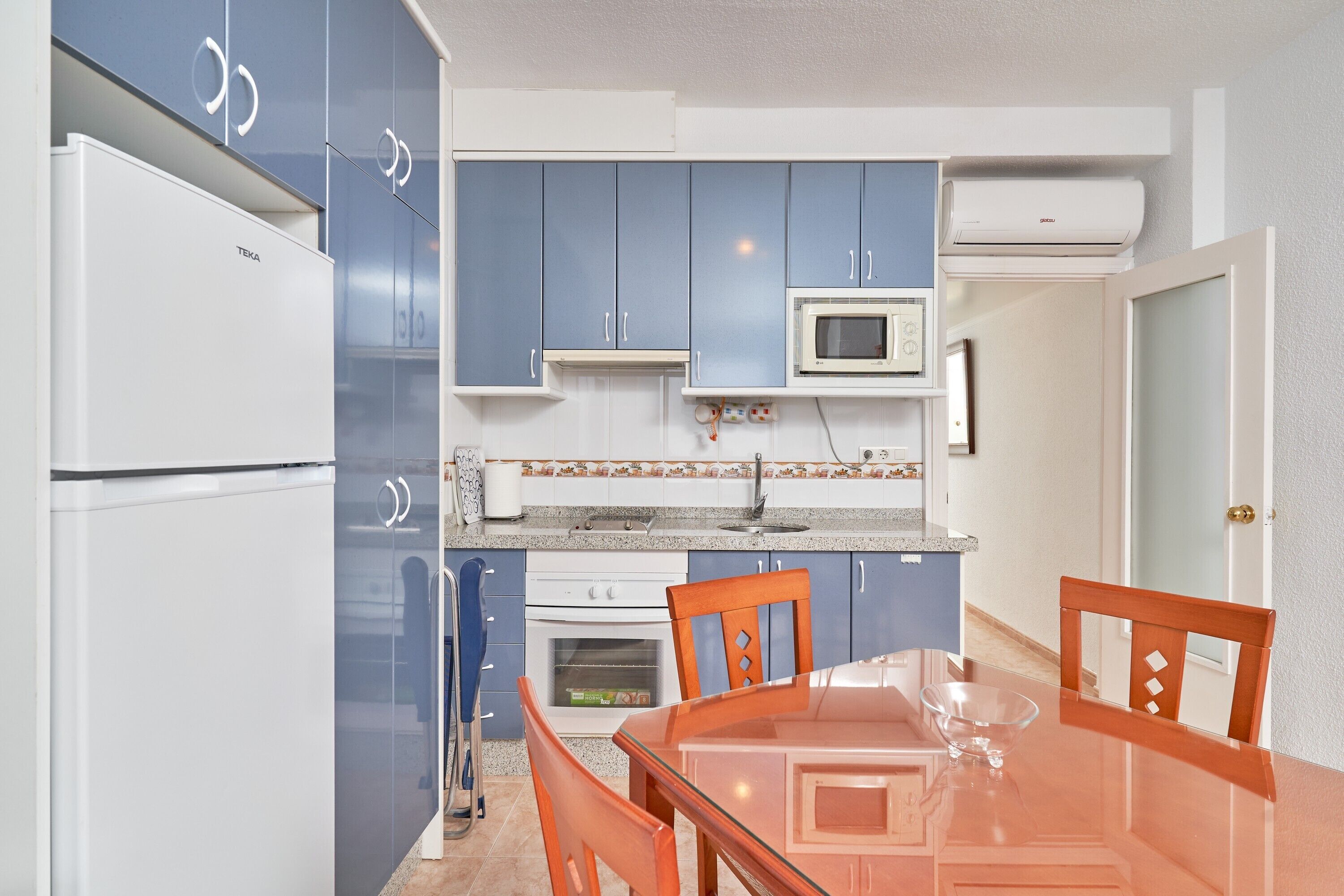A compact kitchen with blue cabinets, a white refrigerator, a microwave, and a dining table with chairs.