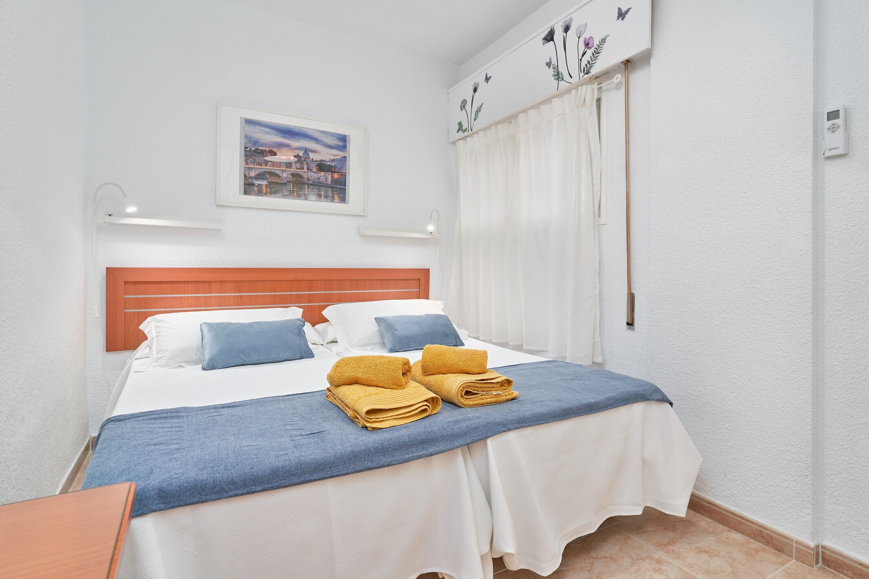 Une chambre d’hôtel avec un lit, des oreillers, une couverture bleue et un tableau au mur.