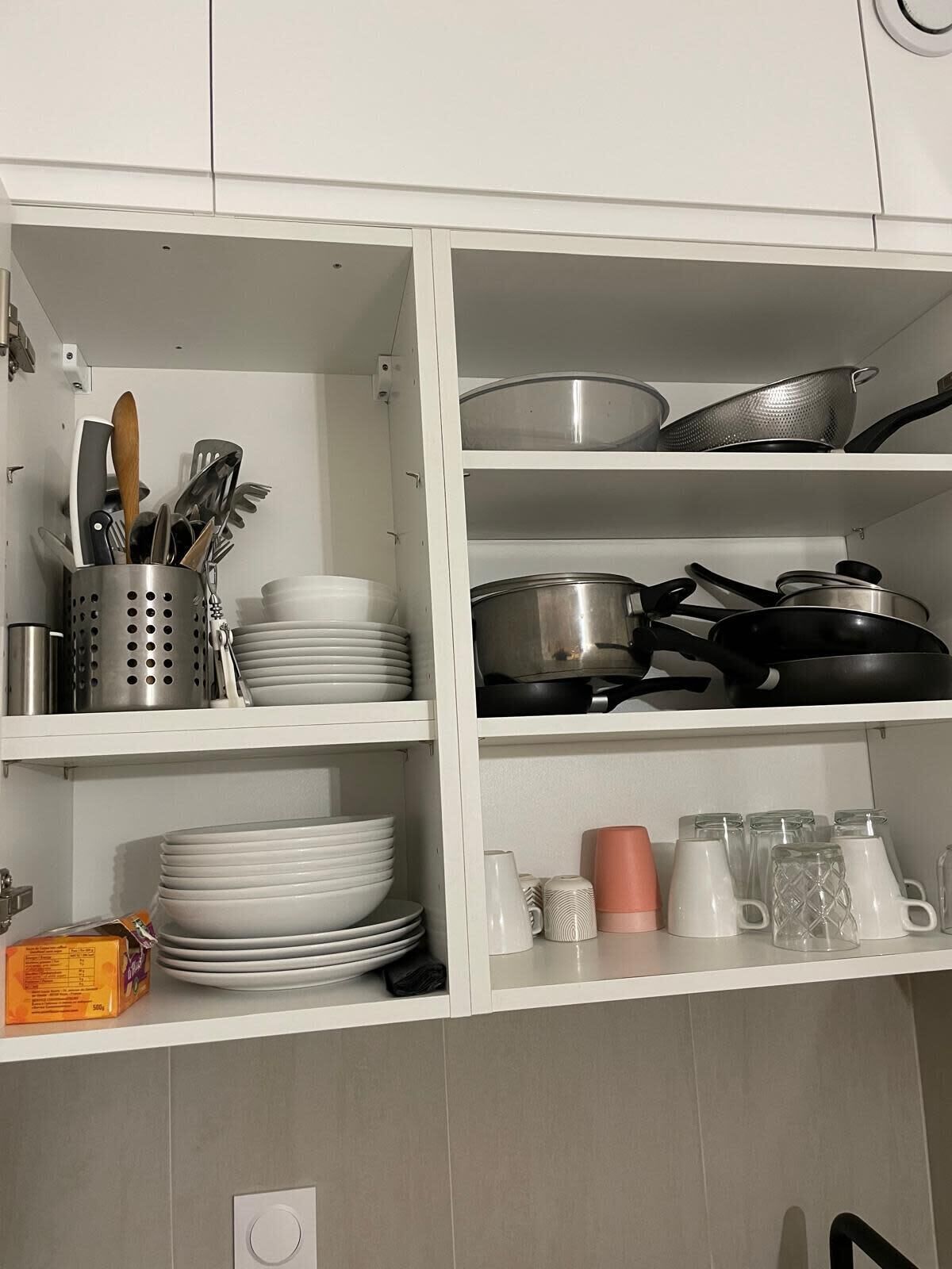 A kitchen with white cabinets, stainless steel cookware, and a variety of dishes and utensils.