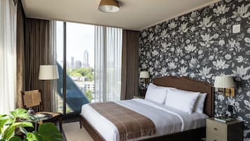 Quarto de hotel com uma cama grande, duas luminárias de cabeceira, vista para a cidade e papel de parede floral.