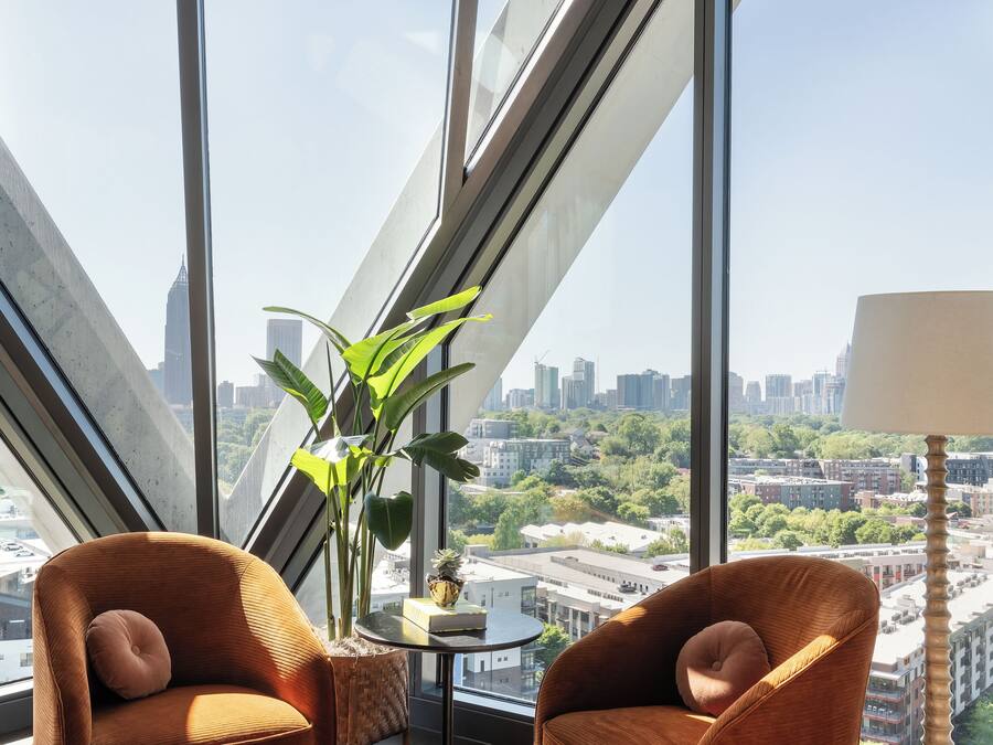 Una habitación moderna con ventanas amplias, dos sillones tapizados en marrón, una mesita y una planta en maceta.