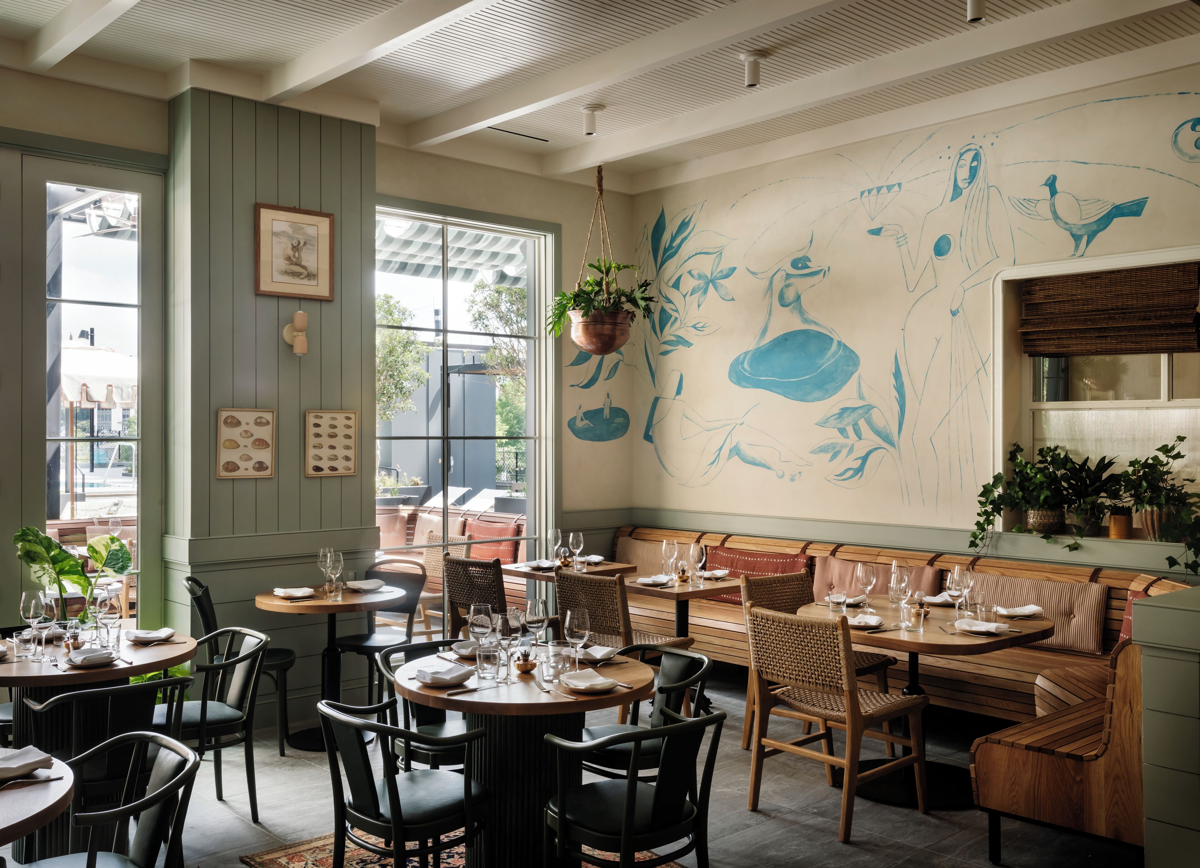 A restaurant interior with round tables, wooden chairs, and a mural on the wall.