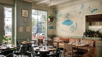 A restaurant interior with round tables, wooden chairs, and a mural on the wall.