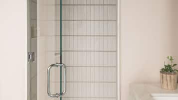 Bathroom features a glass-enclosed shower with a clear door and safety bar, alongside a marble countertop with a sink.