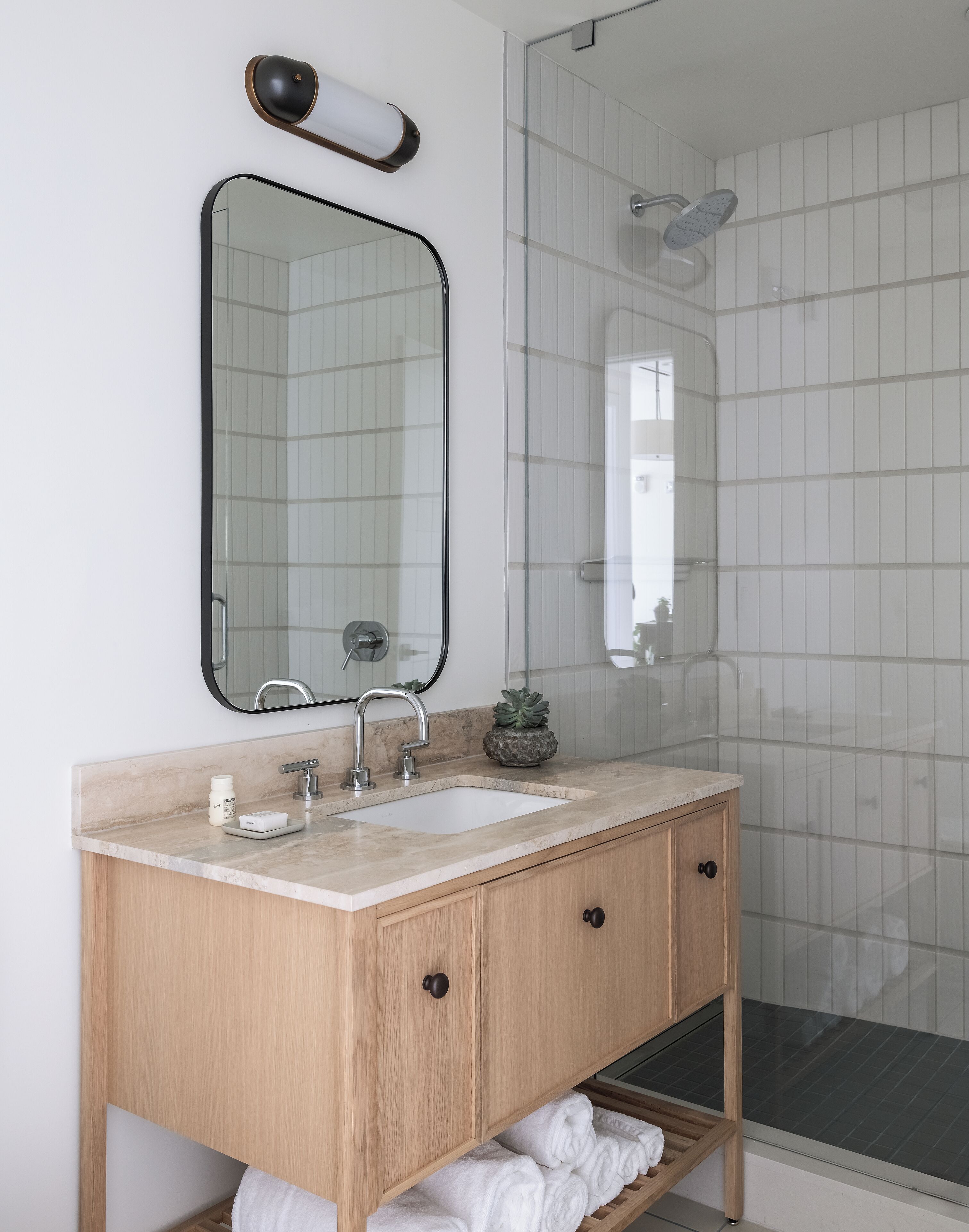 Un baño con tocador de madera, dos lavamanos, un espejo, toallero y zona de ducha.