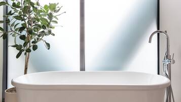 A modern bathroom with a freestanding bathtub, a potted plant, and a shower area.