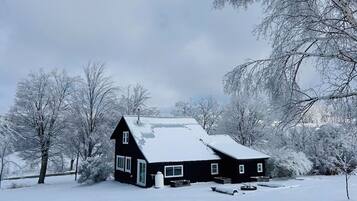 Een huis bedekt met sneeuw, met een donkere gevel, omringd door bomen en een besneeuwd landschap.