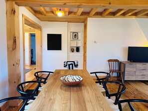 Un comedor con una mesa de madera, sillas negras, un cuenco decorativo y un televisor sobre un mueble de madera.