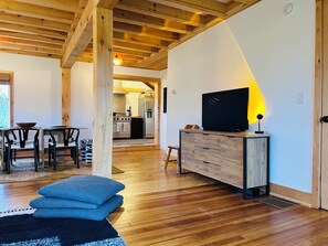 Ett rymligt vardagsrum med ett träpanelat tak, ett matbord med stolar, en soffa och en tv-apparat placerad på ett träskåp.