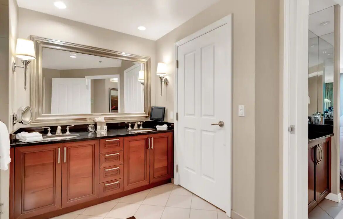 A modern bathroom with a large mirror, wooden cabinets, and a white door.