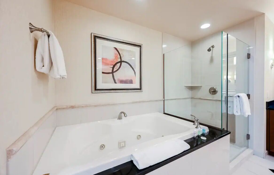 Un baño moderno con una bañera grande, una cabina de ducha con mampara de vidrio y una obra de arte abstracta enmarcada en la pared.