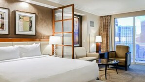 Une chambre d’hôtel avec un grand lit, un bureau, une chaise et une vue sur la ville par la fenêtre.