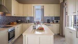 Une cuisine moderne avec des meubles blancs, un îlot central, un four encastré et une fenêtre avec des rideaux.