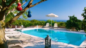 Une piscine entourée de verdure, avec des chaises longues et une lanterne, offrant une vue dégagée sur l’océan.