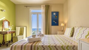 Une chambre d’hôtel avec un lit, une table de chevet, une lampe, une fenêtre avec des rideaux, un tableau et une vue sur la mer.