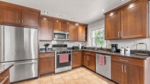 A modern kitchen with stainless steel appliances, wooden cabinets, and a tiled floor.