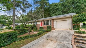 A single-story house with a garage, a front yard with a small tree, and a brick exterior.